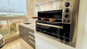 A kitchen with a built-in oven and a window overlooking a cityscape. - Enseada Azul - Beachfront, Luxury (Guarapari)