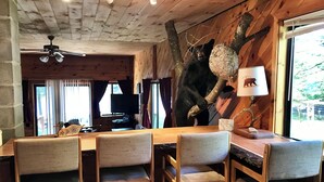 A wooden interior with a dining table and chairs, a ceiling fan, and a bear sculpture on the wall.