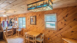 A wooden cabin interior with a dining area, a fireplace, and a large window.