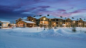 Een besneeuwd resort met meerdere chaletgebouwen, een skilift en een goed onderhouden parkeerplaats.