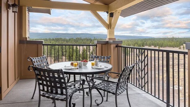 Een overdekt terras met een ronde tafel en vier stoelen, met uitzicht op een bergachtig landschap.