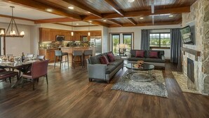 Een ruime woonkamer met een stenen open haard, een eethoek met een houten tafel en stoelen, en een keuken met houten kasten en een stenen aanrecht.