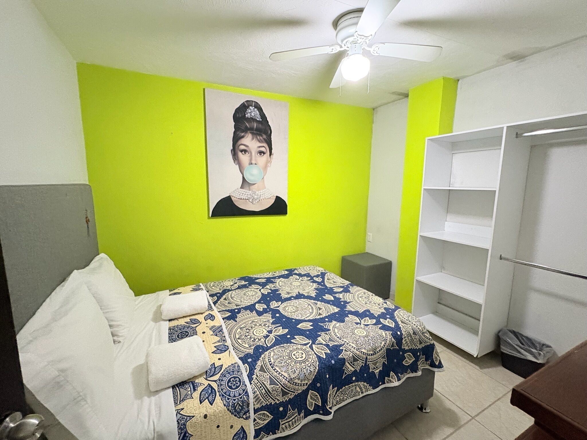 Un dormitorio con cama, armario, ventilador de techo y una pared decorada con un cuadro.