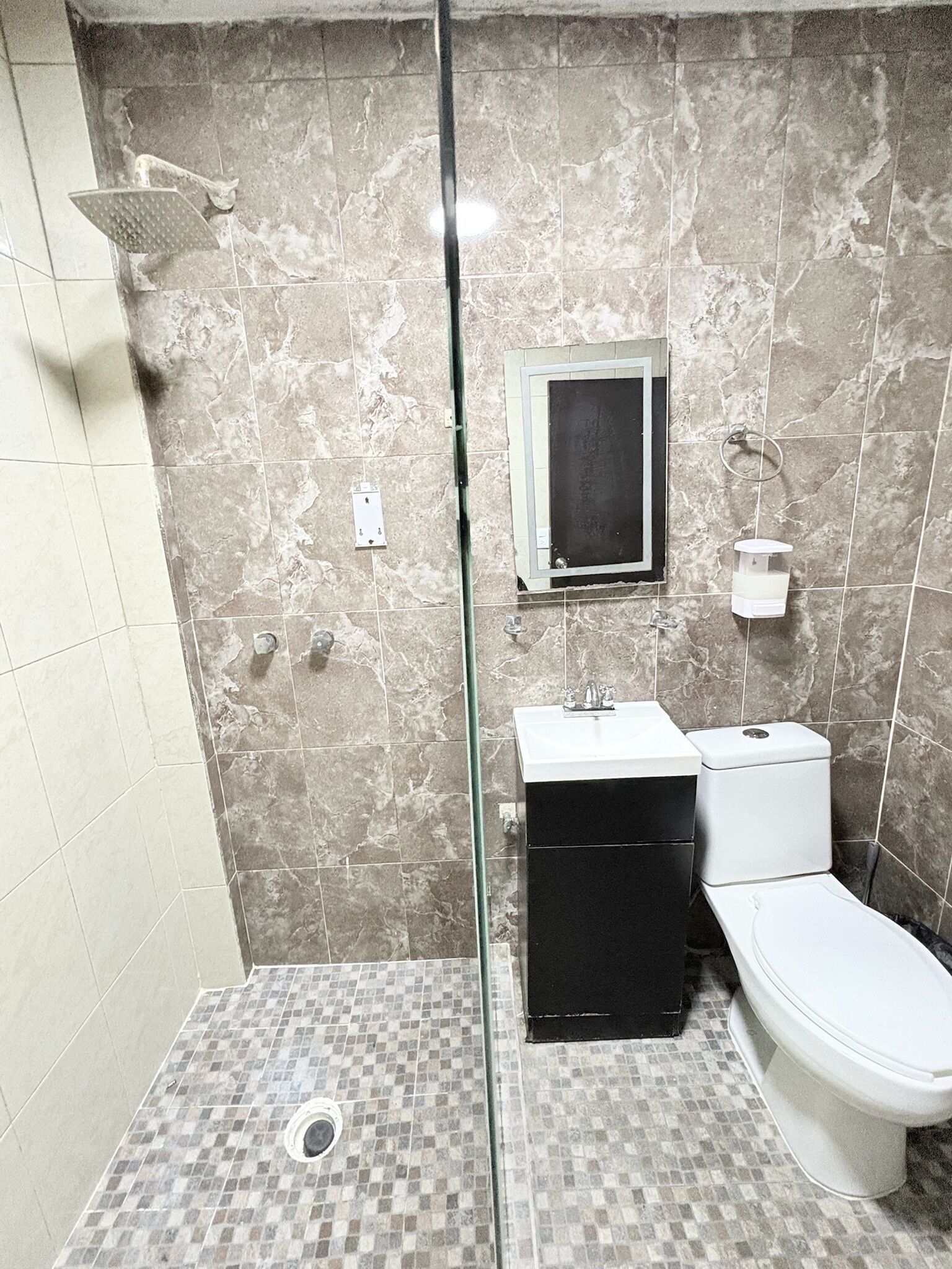 A bathroom with a shower, toilet, sink, and a small window.