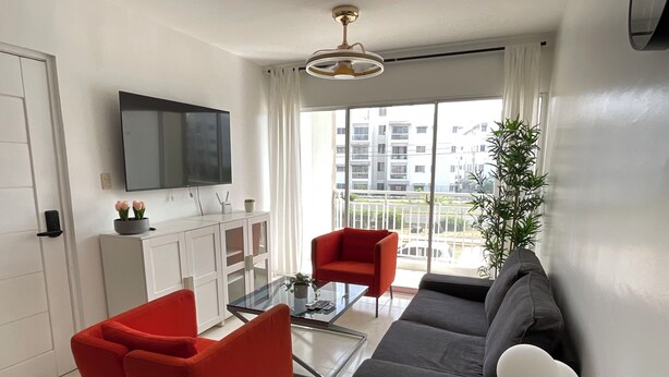 Ein modernes Wohnzimmer mit einer Couch, roten Sessel, einem Glastisch und einem an der Wand montierten Fernseher.