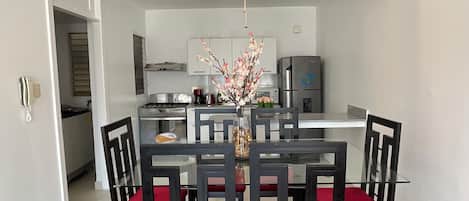 Une cuisine moderne dotée d’appareils électroménagers en acier inoxydable, un coin repas avec une table en verre et des chaises à coussins rouges, ainsi qu’un lustre décoratif.