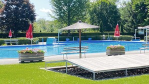 A swimming pool with a wooden deck, red umbrellas, and potted plants. - Ferienhaus in Foetschach (Leutschach an der Weins)