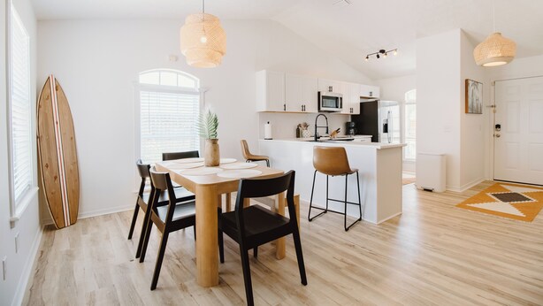 A modern kitchen with white cabinets, a microwave, and a dining area with a wooden table and chairs. - 30A Oasis with Lake, Beach, Patio, Fenced Yard for Pets (Panama City Beach)