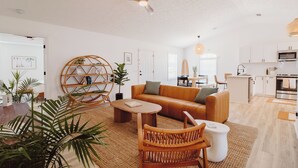 A modern living room with a sofa, coffee table, and wicker chairs. There is a ceiling fan, a dining area with a table and chairs, and a kitchen area with cabinets and appliances. - 30A Oasis with Lake, Beach, Patio, Fenced Yard for Pets (Panama City Beach)