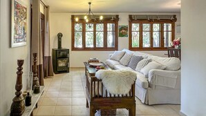 Una sala de estar con un sofá blanco, una silla de madera, una chimenea y ventanas amplias.