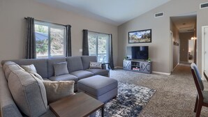 A modern living room with a grey sectional sofa, a small ottoman, a wooden coffee table, and a flat-screen TV on a grey cabinet. - Gated Villa Near Bass Lake, Oakhurst, Mariposa, Yosemite with HotTub, EV Charger (Ahwahnee)