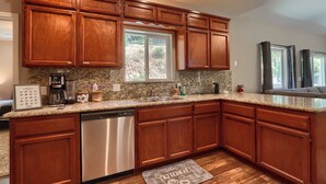 A kitchen with wooden cabinets, granite countertops, a dishwasher, and a window with a view of the outdoors. - Gated Villa Near Bass Lake, Oakhurst, Mariposa, Yosemite with HotTub, EV Charger (Ahwahnee)