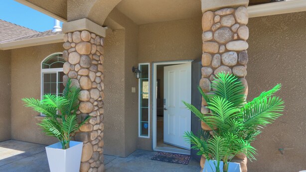 A building entrance with a stone pillar, a door, and two potted plants. - Gated Villa Near Bass Lake, Oakhurst, Mariposa, Yosemite with HotTub, EV Charger (Ahwahnee)