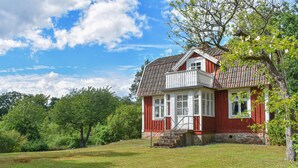 A red wooden house with a white balcony, surrounded by lush greenery and trees. - Cozy home in Mörrum with WiFi (Mörrum)