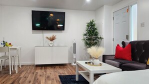 A modern living room with a flat-screen TV mounted on the wall, a white cabinet, a small table with a vase, a tall plant, and a sofa with red and yellow cushions. - Studio Room in Halifax (Halifax)