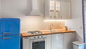 A compact kitchen with white cabinets, a blue refrigerator, a gas stove, and a sink.