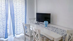 A dining area with a white table, blue-striped curtains, a TV, and a blue vase.