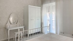 A bedroom with a bed, a dresser with a mirror, a small table, and a window with curtains.