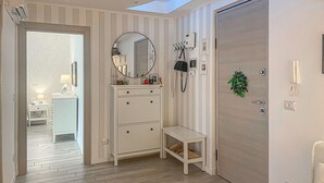 A room with a wooden floor, a white vanity with drawers, a mirror, a small bench, a door with a wreath, and a phone on the wall.