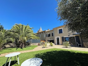 A courtyard with a palm tree, a white table, and a building with a stone facade and a conical roof. - Gîte La Vade Carcassonne (Carcassonne)
