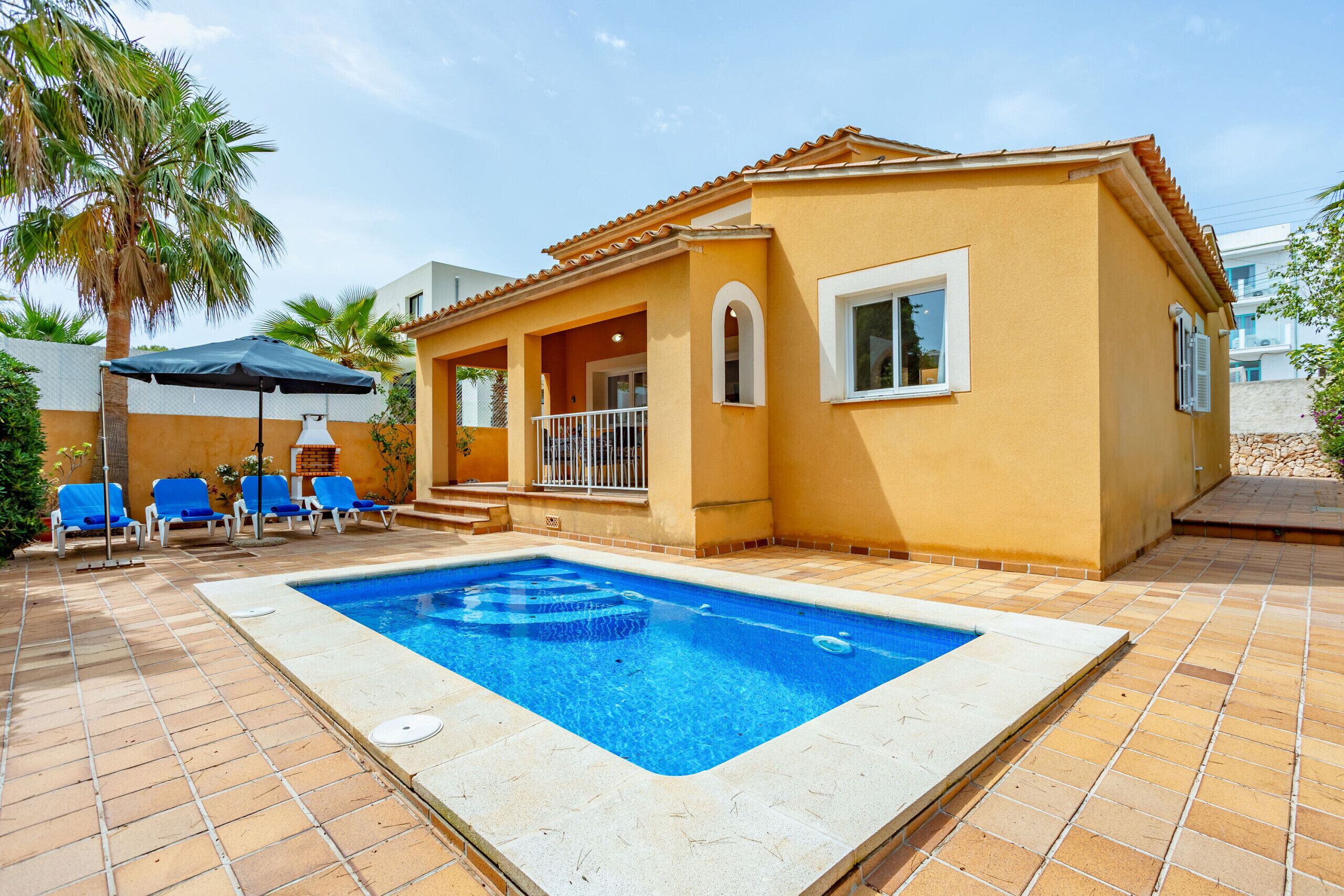 Propiedad residencial con piscina, sillones azules y patio con baldosas.