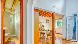 A bathroom with a toilet, shower, and sink; a dining area with a table and chairs; and a bedroom with a bed and window. - Casa Tulipa by dracmallorca (Cala Llombards)