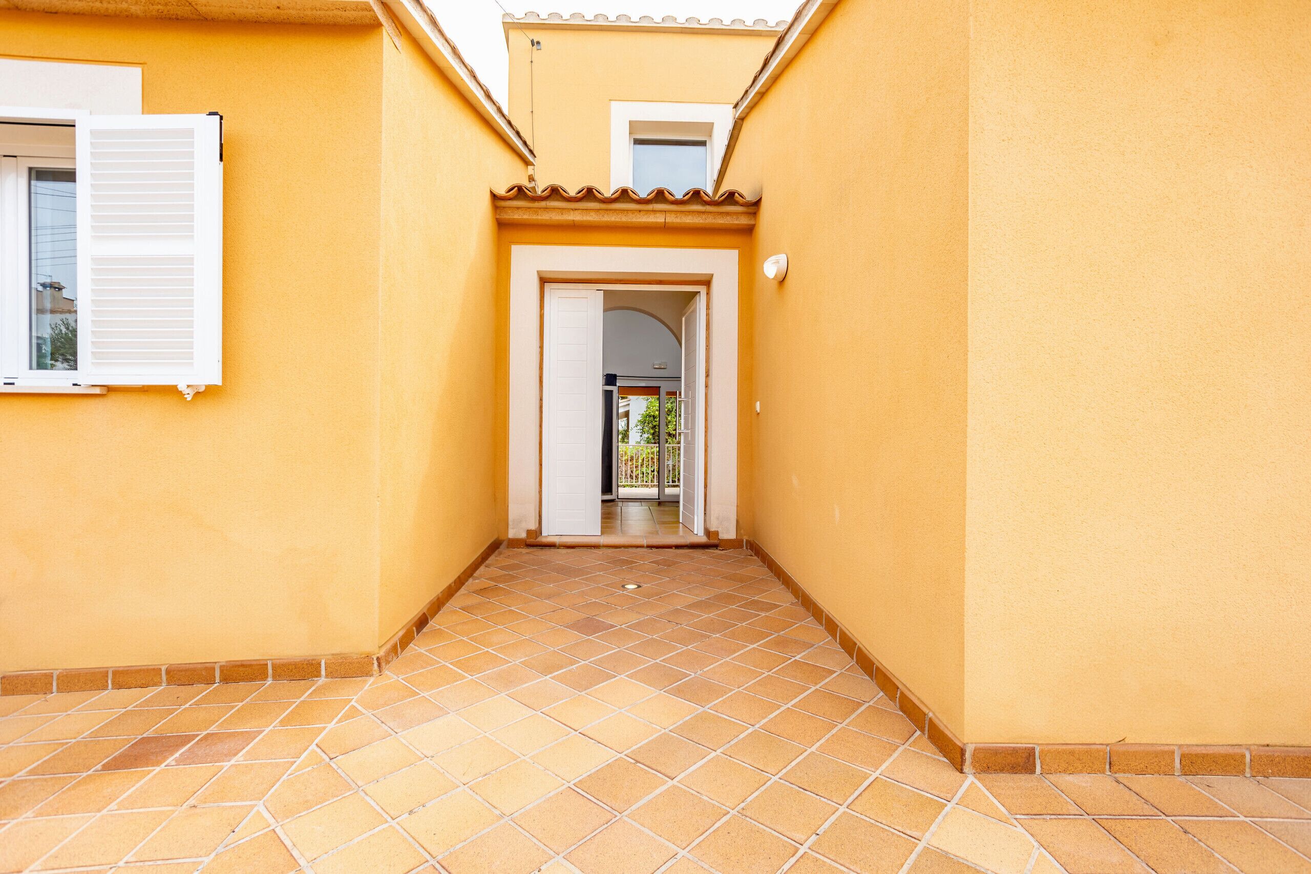 A corridor with tiled flooring, a door leading to a balcony, and a window with shutters.