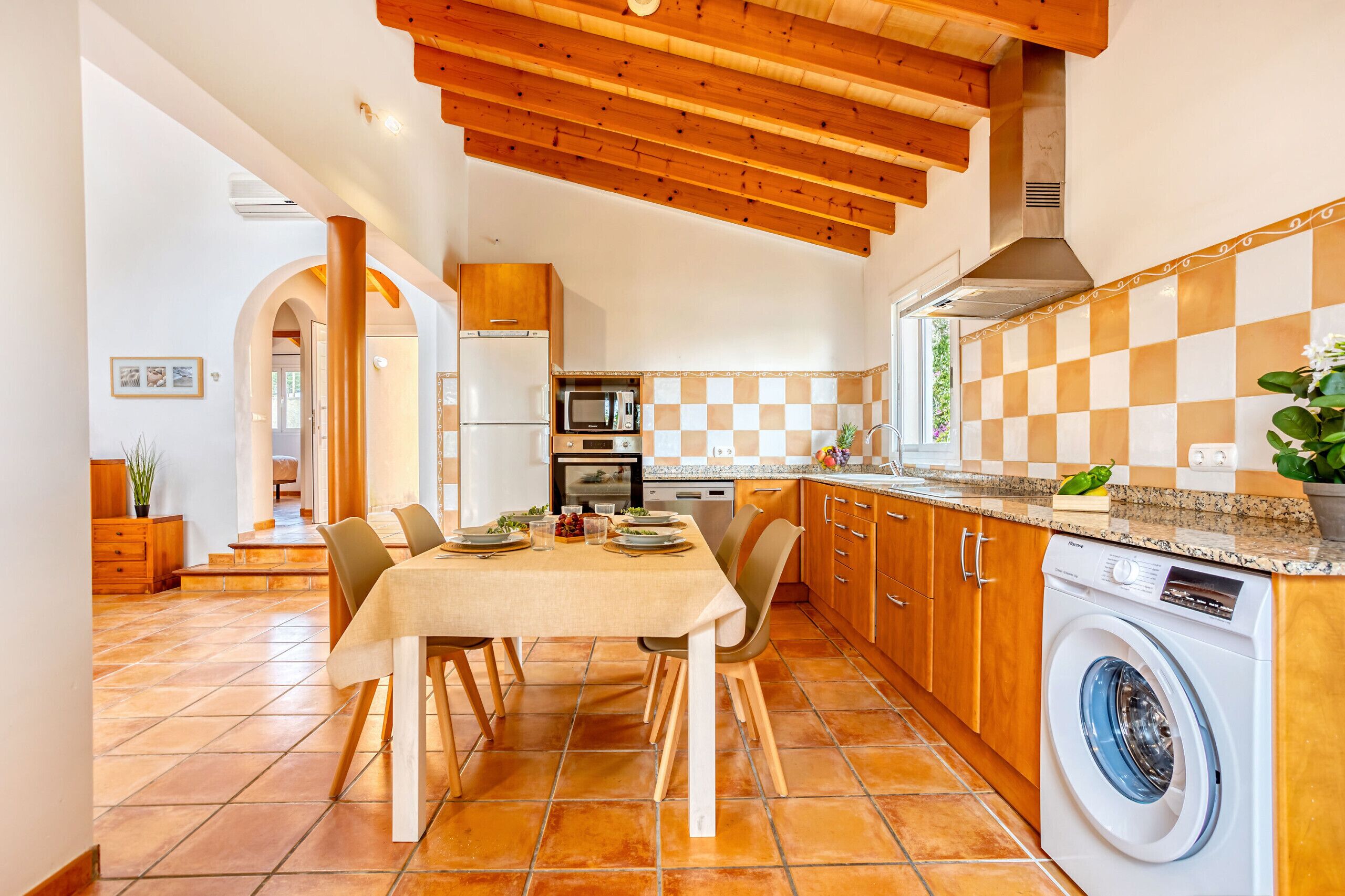Une cuisine avec une table à manger, des meubles de rangement en bois, un lave-linge et un crédence à carreaux.