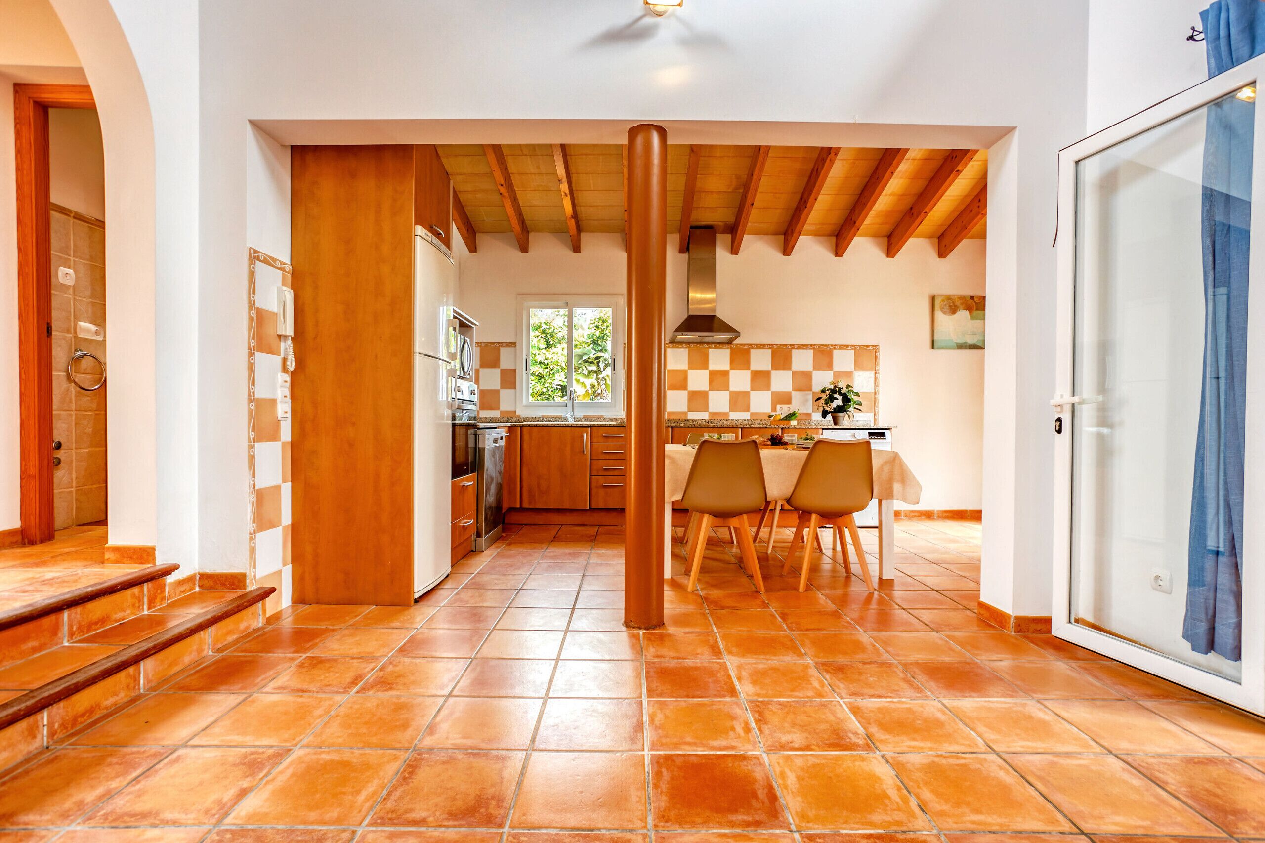 A spacious kitchen with wooden beams, a dining area with chairs, and a view of the outdoors.