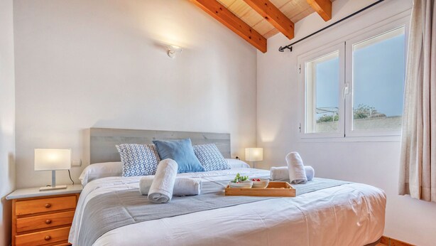 A bedroom with a bed, bedside tables, a window with curtains, and a view of the beach. - Casa Tulipa by dracmallorca (Cala Llombards)