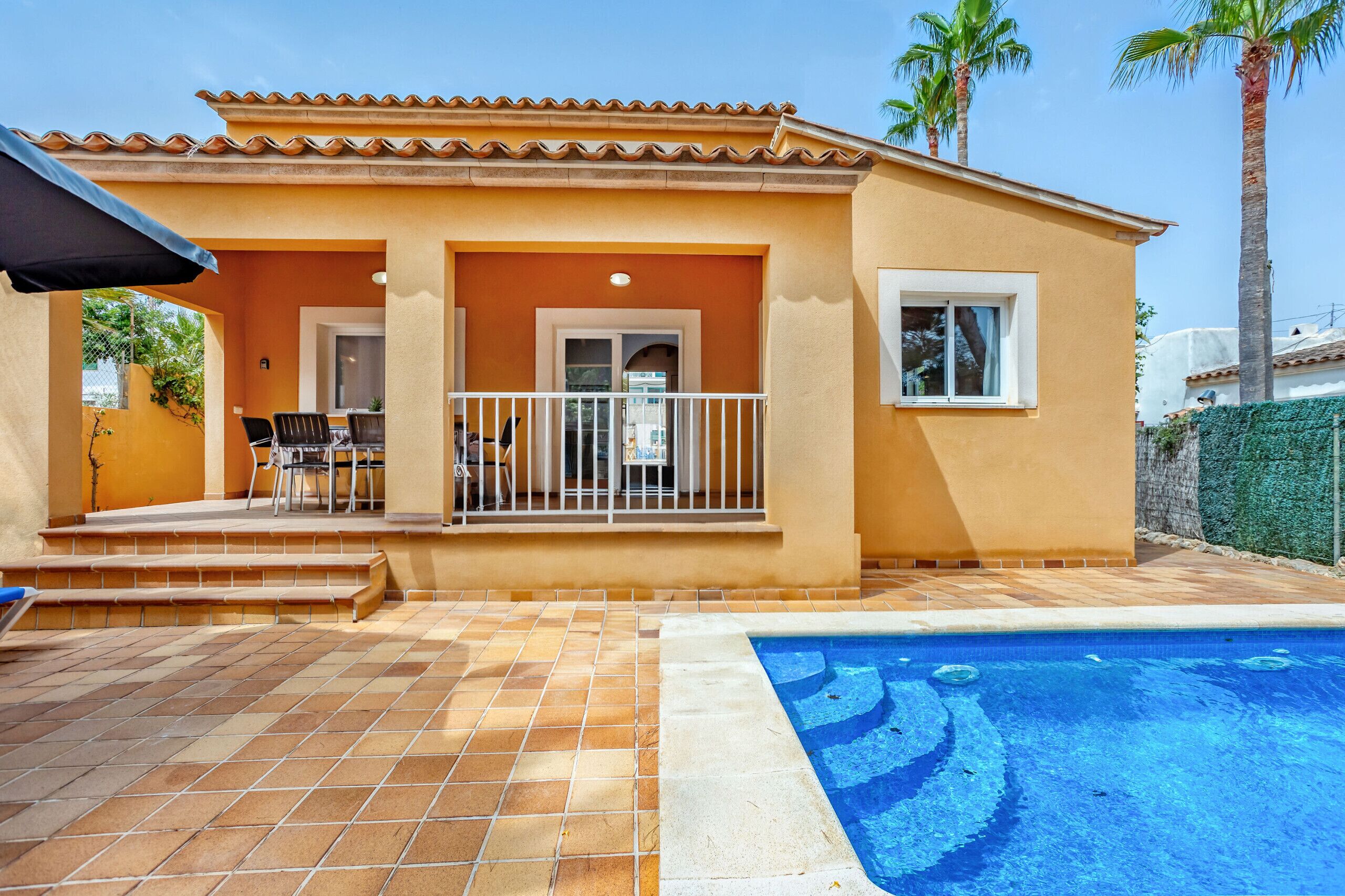 Une maison avec une piscine, une terrasse avec des chaises et un petit balcon.