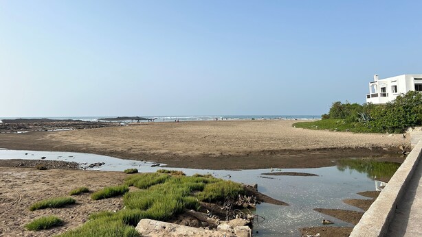 Une plage avec un bâtiment blanc, une barrière en béton et un ciel dégagé.