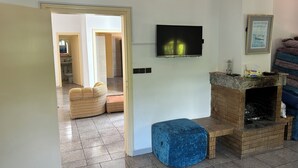 Un salon avec un téléviseur fixé au mur, une cheminée et un pouf bleu.