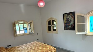 Une chambre à coucher avec un lit, deux fenêtres, un tableau et un luminaire rouge suspendu au plafond.