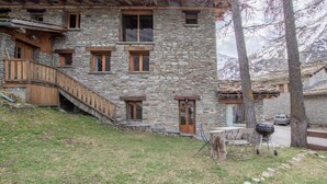 A stone building with a wooden staircase, a barbecue grill, and a car parked in the background. - LES FLOCONS - BONNEVAL SUR ARC (BONNEVAL SUR ARC)