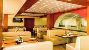 Un restaurant avec des banquettes, un téléviseur fixé au mur et une grande fenêtre en arc de cercle.