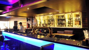 Un espace bar comprenant un comptoir, des tabourets de bar et des étagères remplies de verres.