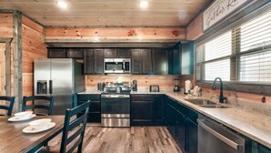 A modern kitchen with wooden accents, stainless steel appliances, and a dining area with a table and chairs. - Free Dollywood Tix/10Min2Dollywood/DogsOK (Sevierville)