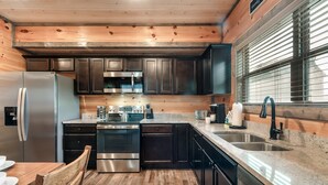 A modern kitchen with dark cabinets, stainless steel appliances, a granite countertop, and a wooden dining table.