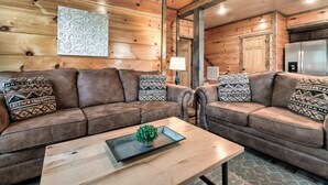 A cozy living room with two brown sofas, patterned cushions, a wooden coffee table with a plant, and a modern kitchen in the background.