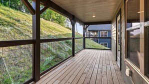 A wooden deck with a metal railing, overlooking a grassy hill and a house.