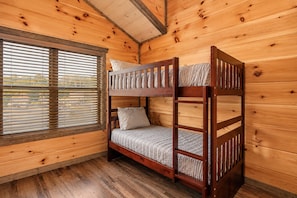 A bunk bed room with wooden walls and a window with blinds.
