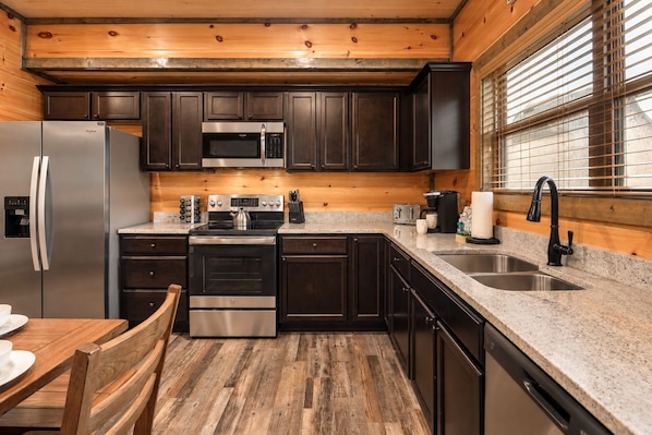 A modern kitchen with dark cabinets, stainless steel appliances, a granite countertop, and a wooden floor.