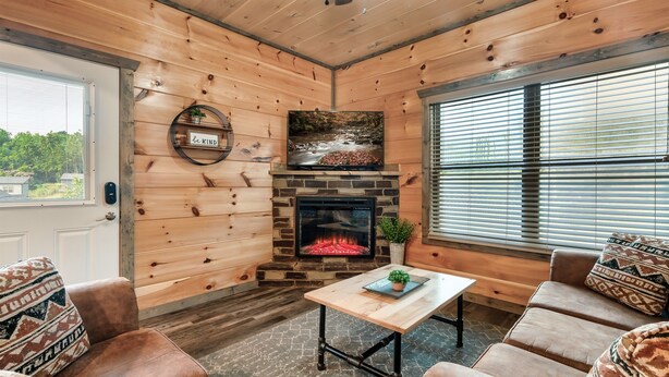 A cozy cabin interior with a stone fireplace, wooden walls, and a comfortable seating area.