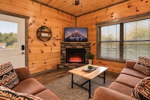 A cozy cabin interior with a fireplace, wooden walls, a sofa, and a television.