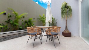 Eine Terrasse mit Korbstühlen, einem runden Tisch und einem Blumentopf.