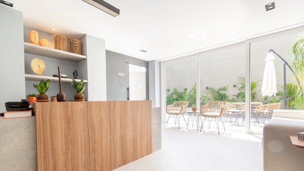 Ein moderner Empfangsbereich mit einem Holzbüro, Regalen mit Dekoration und Blick auf eine Terrasse mit Sitzgelegenheiten und Pflanzen.