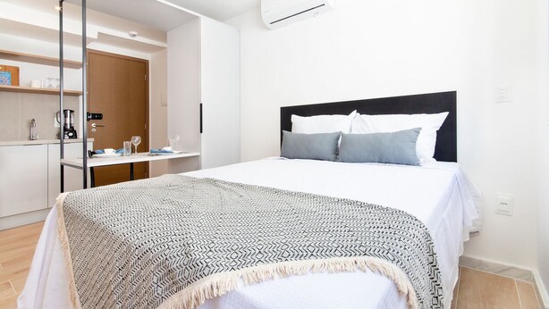 Ein modernes Hotelzimmer mit einem großen Bett, einem Nachttisch, einer Klimaanlage und einem Kleiderschrank.
