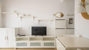Ein modernes, minimalistisches Wohnzimmer mit Flachbildfernseher, weißen Schränken und einem Essbereich.