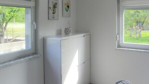 Ein Zimmer mit einem weißen Schrank, zwei gerahmten Bildern an der Wand und einem Fenster mit Blick auf Grünflächen.
